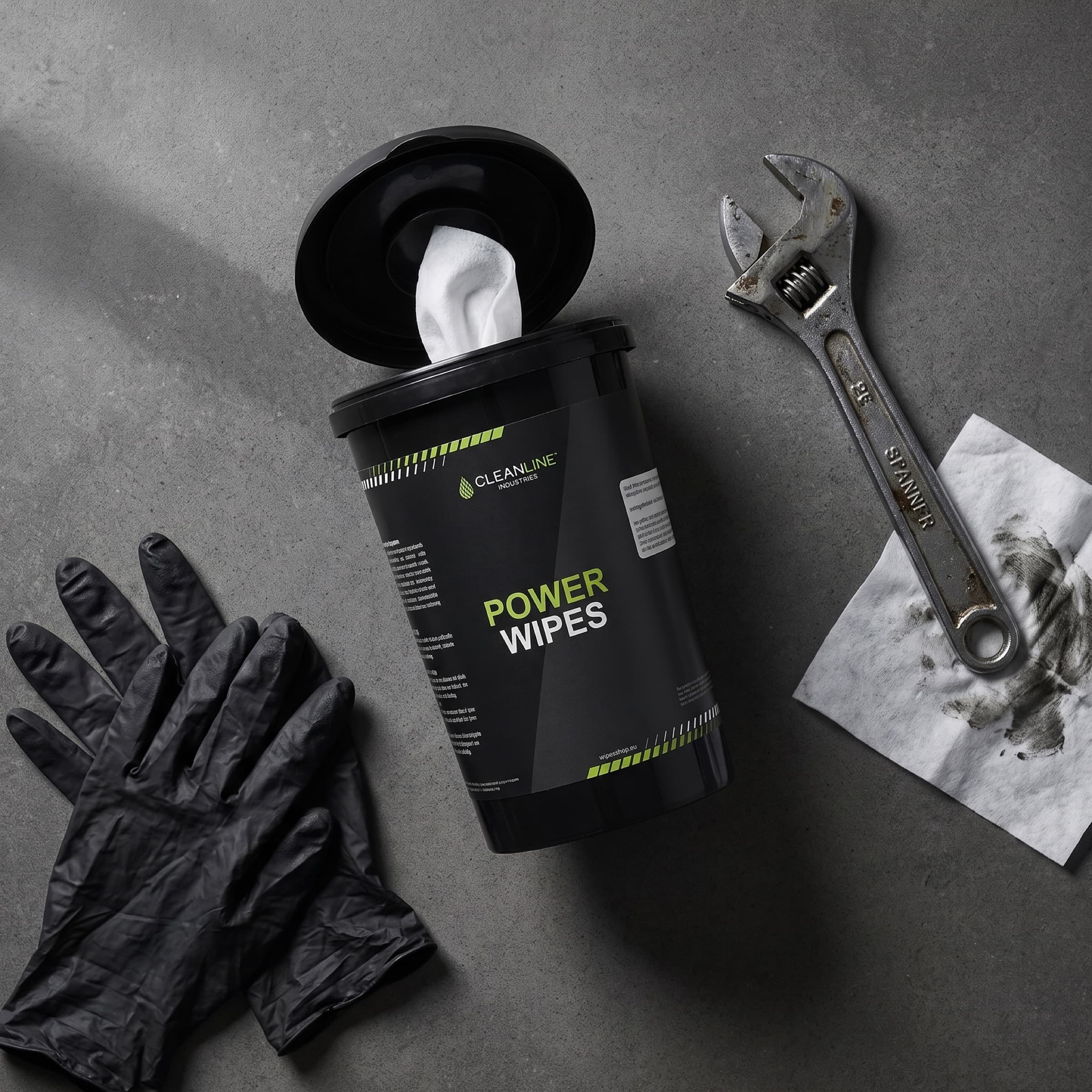 Open tub of Power Wipes with a wrench, nitrile gloves and a used wipe on concrete